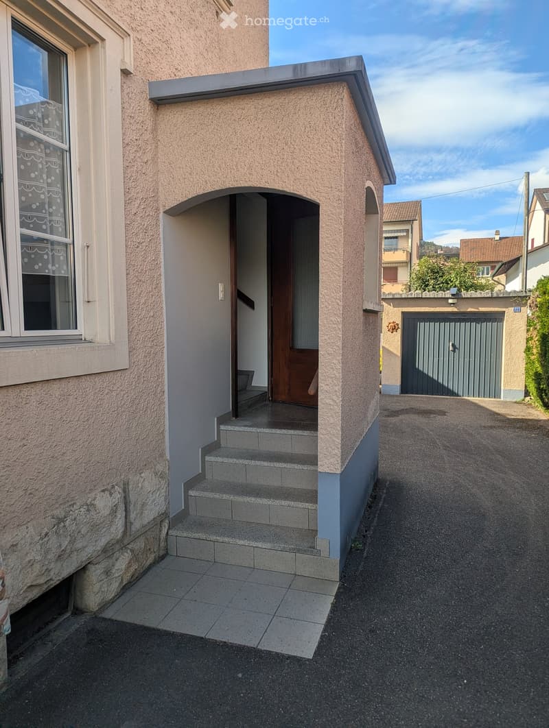 Entrance to a house with a small porch, steps, and a garage visible in the background.