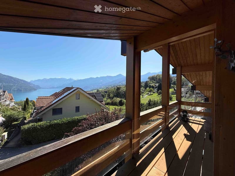 Wooden balcony with a railing, overlooking a scenic lake and mountain landscape.