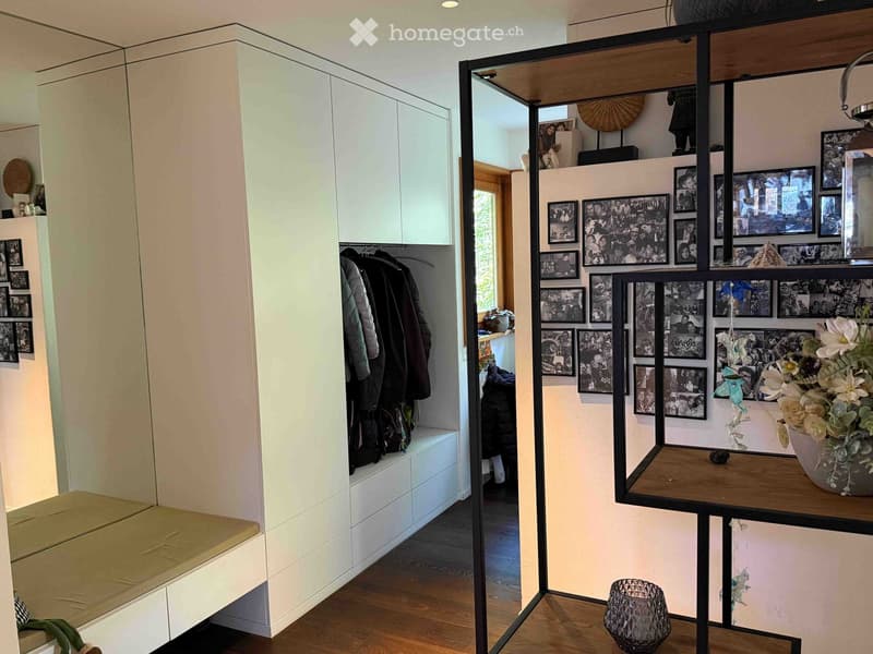 A modern hallway with a built-in bench, white cabinetry, a large mirror, and a wall of family photos displayed on a wooden shelf.