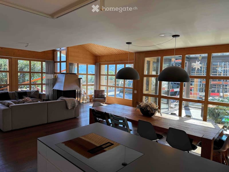 Open-concept living and dining area with large windows, wooden floors, a sectional sofa, dining table with chairs, and a fireplace.
