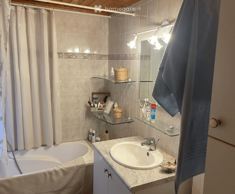 Bathroom with a bathtub, sink, mirror, shelves, and various toiletries including a towel, toothbrush, toothpaste, shampoo, and soap.