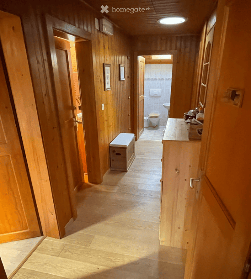 Wooden-paneled hallway with a bench, leading to a bathroom with a toilet and sink.