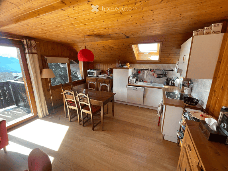 Cozy, wooden-paneled room with a dining area and kitchen. Features a wooden dining table with chairs, a refrigerator, microwave, dishwasher, and cabinets. Large windows offer a scenic mountain view.