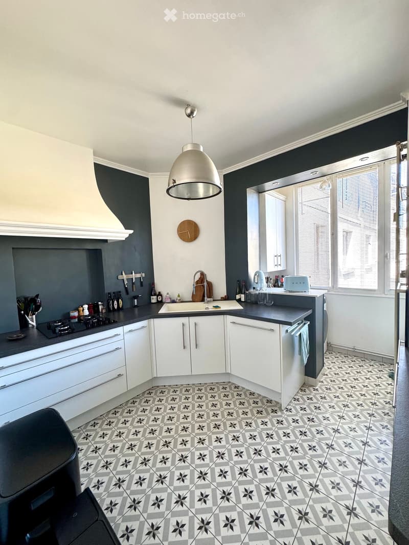Modern kitchen with white cabinets, dark countertops, and patterned tiles. Features a central island with sink and faucet, stove, and various appliances.
