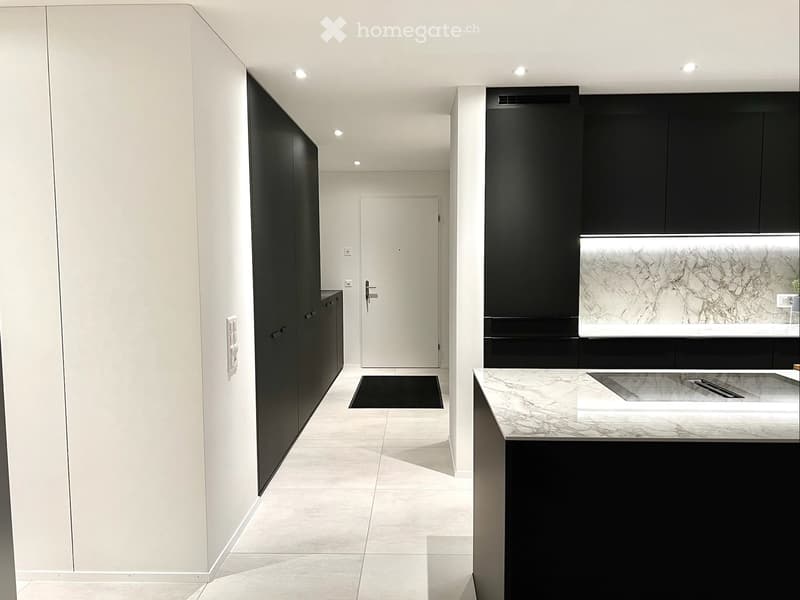Modern hallway with white walls, light-colored tiled floor, black cabinets, and a white door leading to another room.
