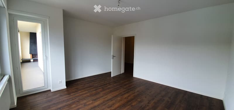 Empty room with wooden flooring, white walls, and two open doors leading to adjacent spaces.