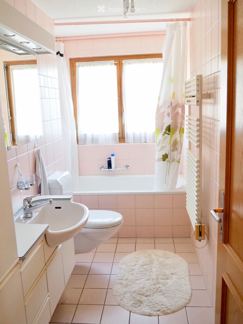 Bathroom with a white sink, toilet, bathtub, mirror, and a white fluffy rug on the floor.