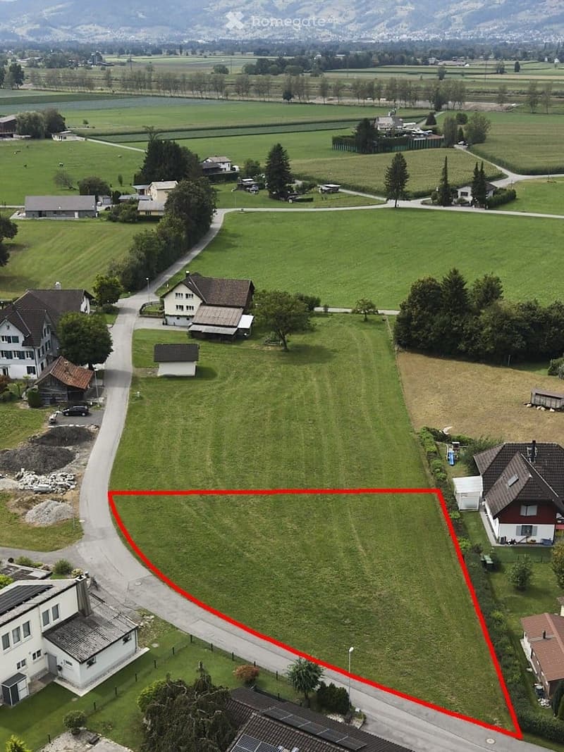 Aerial view of a rural area with multiple houses, green fields, and a road running through the landscape.