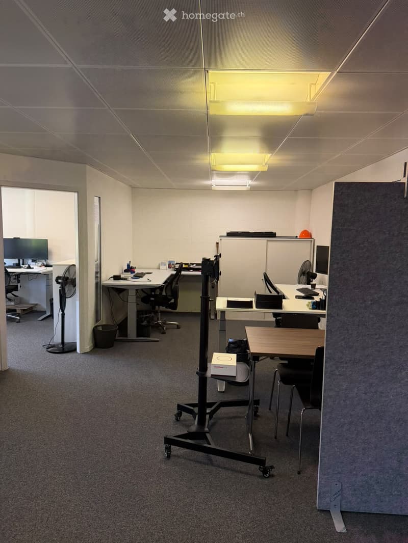 Office space with multiple desks, chairs, computers, fans, and a small table with chairs.