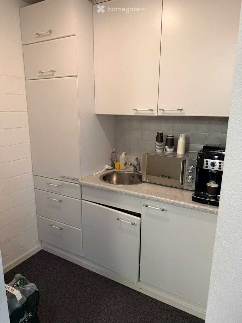 Compact kitchen with white cabinets, a stainless steel sink, microwave, coffee maker, and several cups on the counter.