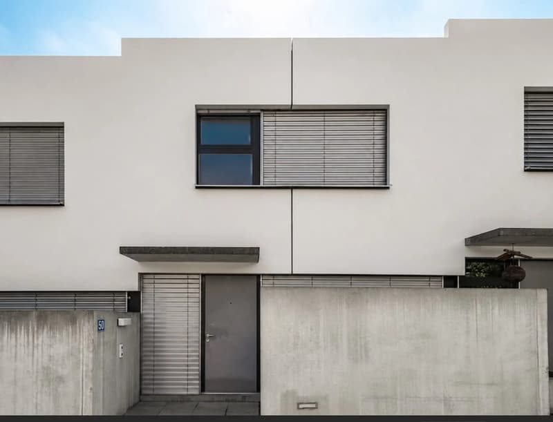 Modern two-story house with white walls, large windows with blinds, and a concrete garage entrance.