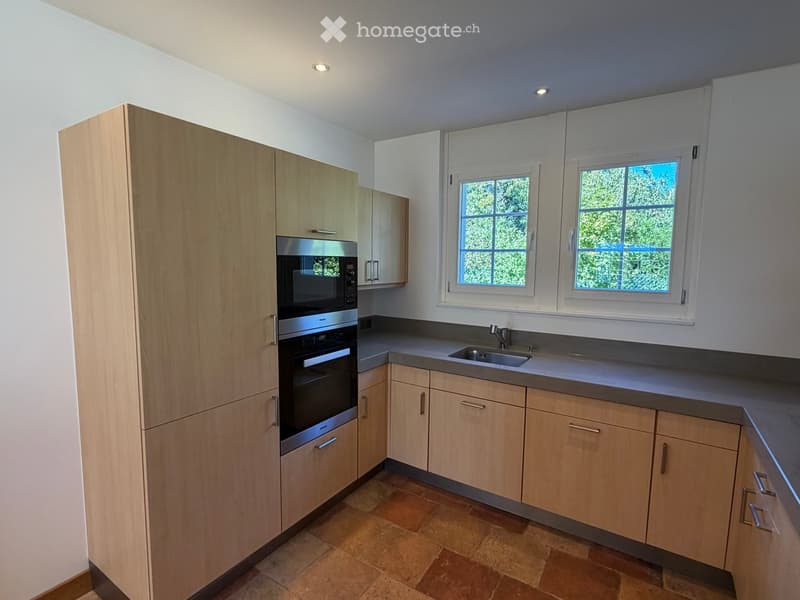 Modern kitchen with light wooden cabinets, stainless steel appliances, and a tiled floor.