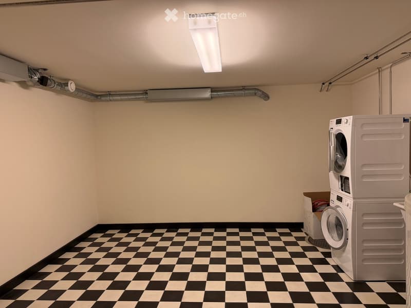 Clean, well-lit laundry room with black and white checkered flooring, white walls, and a stacked washer and dryer unit.