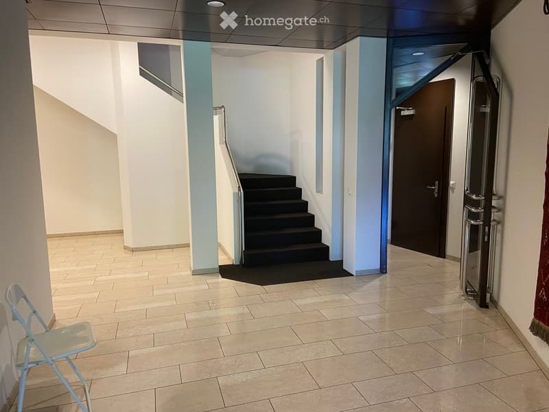 Empty hallway with tiled floor, white walls, a staircase with black steps, and a closed door on the right side.