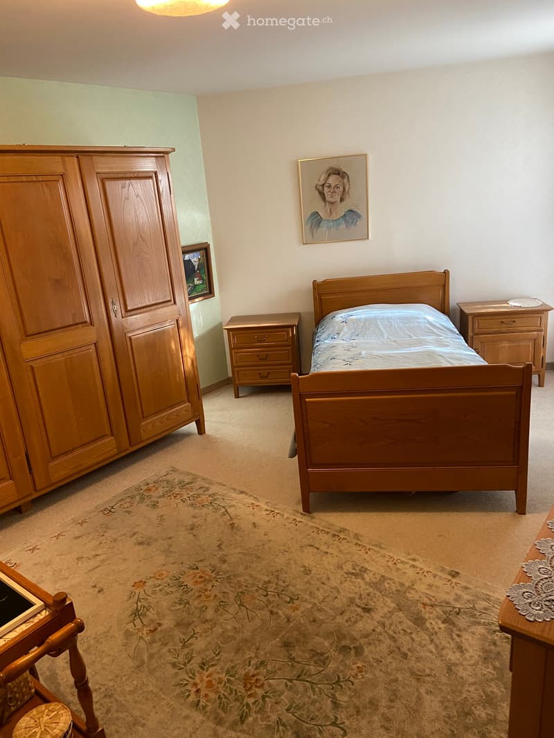 Cozy bedroom with a wooden bed, nightstands, dresser, and a floral rug on the floor.