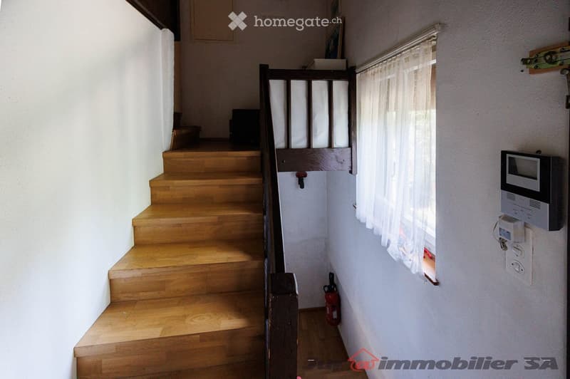 Wooden staircase with a dark wooden handrail, white walls, a window with sheer curtains, a fire extinguisher, and an intercom system mounted on the wall.