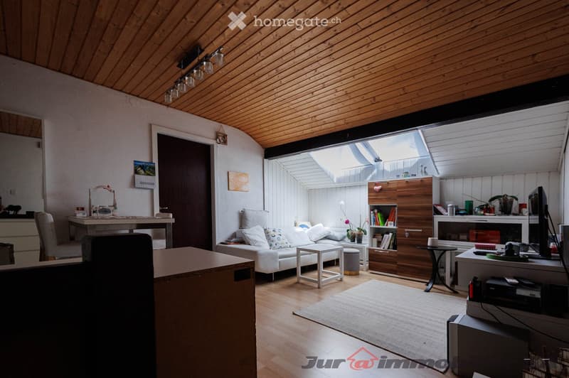 Bright, modern living room with wooden ceiling and floor, large skylight, white sofa, coffee table, bookshelf, TV, and various decorative items.