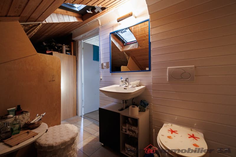 Cozy bathroom with wooden walls, a sink, a mirror, a toilet, a small stool, and a basket on the counter.