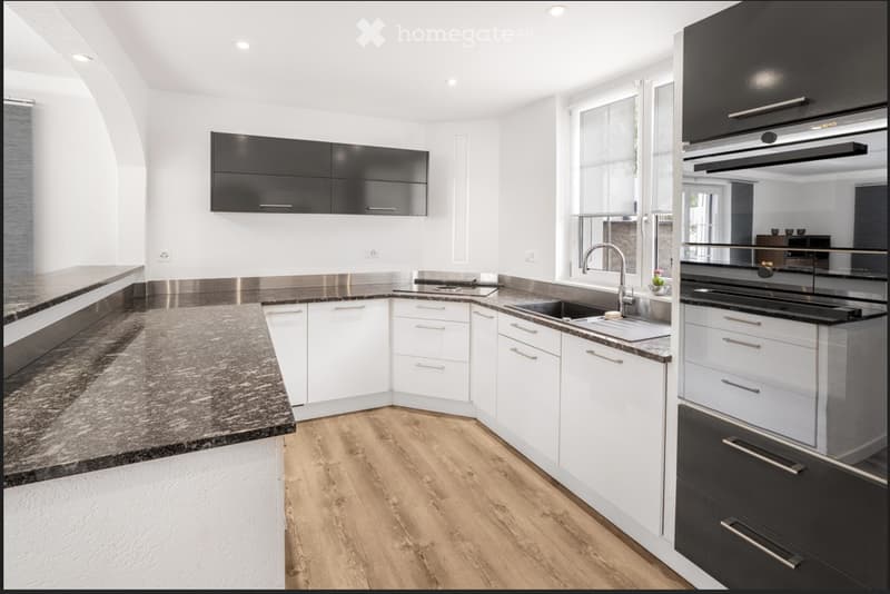 Modern kitchen with white and black cabinets, granite countertop, stainless steel sink, and built-in oven.