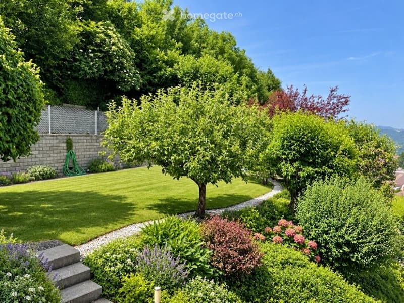 Well-maintained garden with a neatly trimmed lawn, various trees, shrubs, and flowering plants. A gravel pathway winds through the garden, and a small staircase leads up to a higher level.