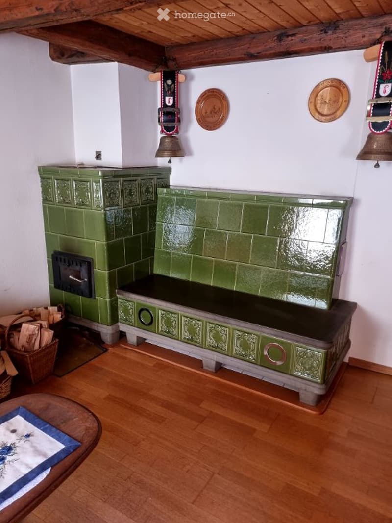 Traditional room with green tiled fireplace, wooden bench, small wooden table, and decorative wall plates.