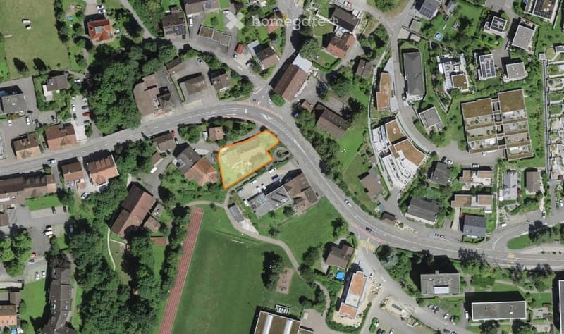 Aerial view of a residential area with multiple houses, roads, and green spaces. The highlighted area in orange suggests a specific plot or property of interest.