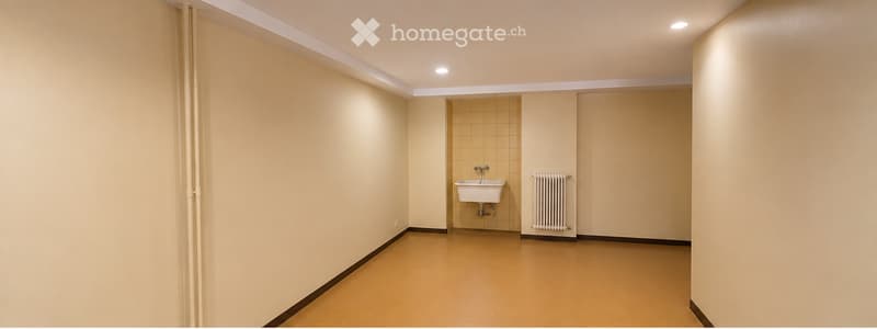 Empty room with beige walls, tiled section, sink, radiator, and light fixtures.