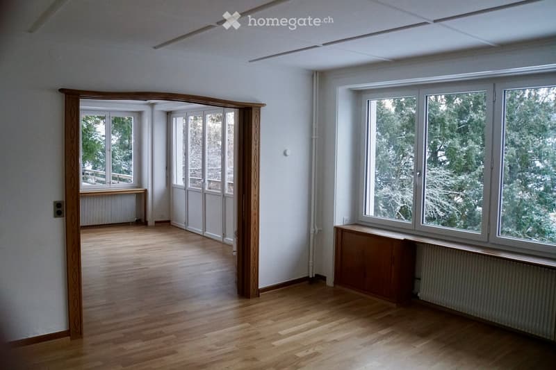 Empty room with wooden flooring, large windows, and sliding glass doors leading to a balcony area.