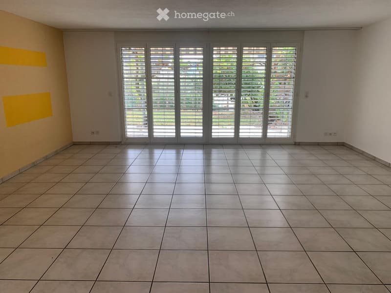 Empty room with tiled floor, large sliding glass doors with blinds, and neutral-colored walls.
