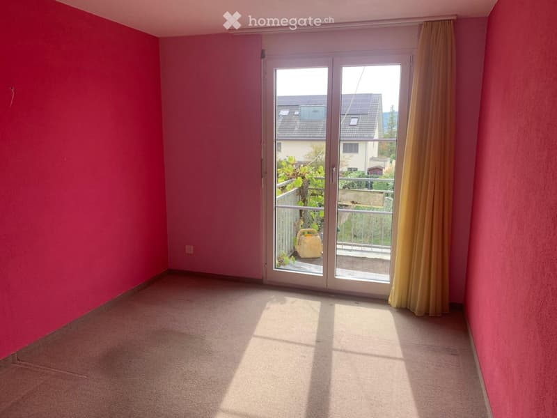 Empty room with pink walls, carpeted floor, large sliding glass door leading to a balcony, and yellow curtain on one side.