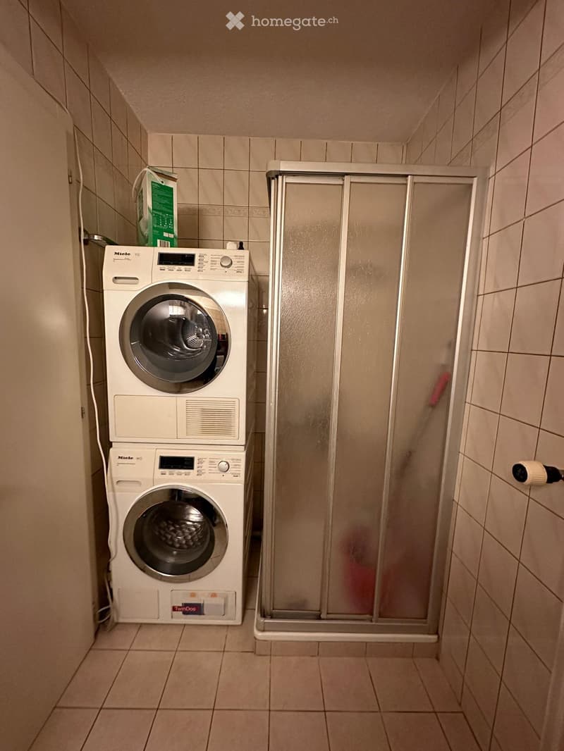 Bathroom with a washing machine and a shower stall.