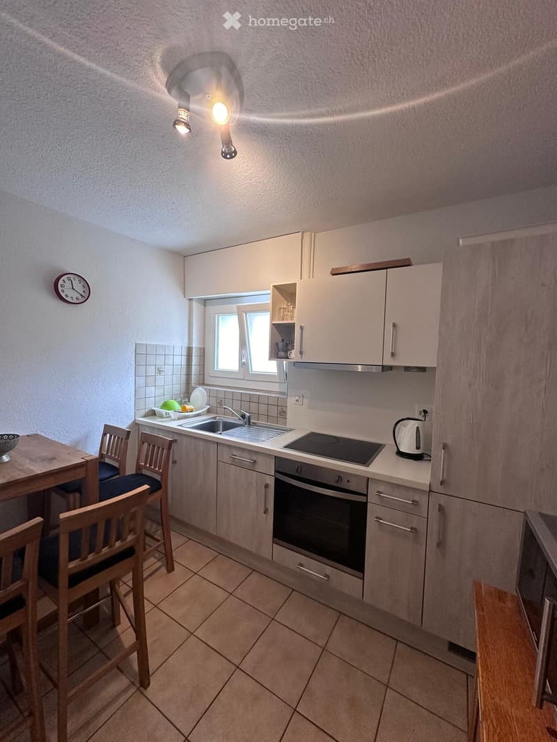 Modern kitchen with light-colored cabinets, a sink, an induction stove, an oven, and a small dining area with a table and chairs.