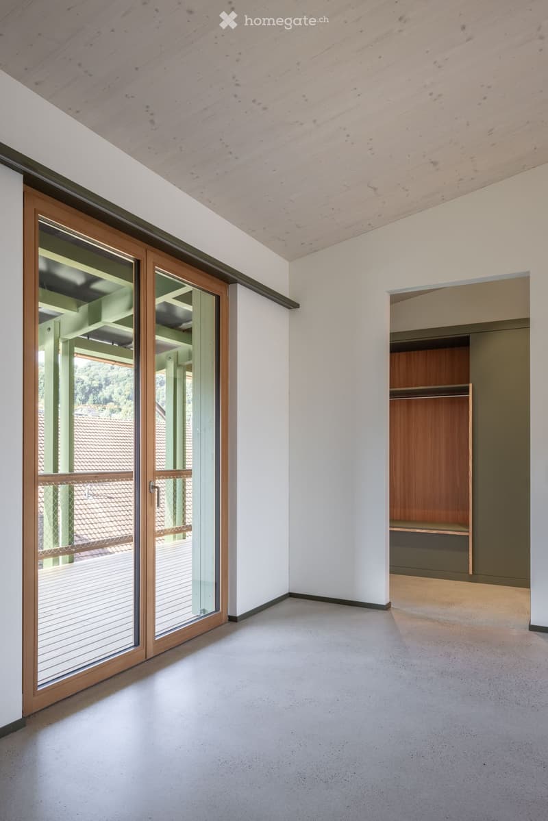 Empty room with white walls, light wooden ceiling, large sliding glass door leading to a balcony, and a built-in wooden closet with shelves.