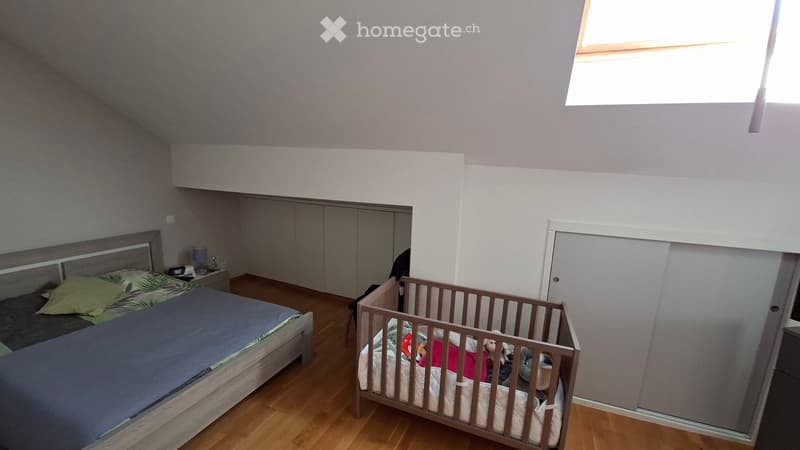 Bedroom with a double bed, crib, nightstand, lamp, and built-in wardrobe. The room features wooden flooring and a skylight window.