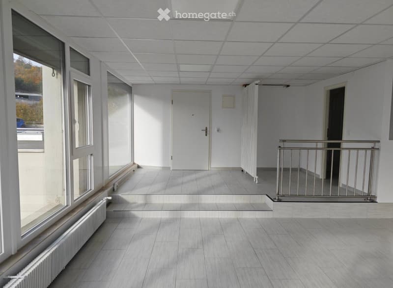 Empty hallway with tiled floor, white walls, large windows, and a metal railing leading to another area.