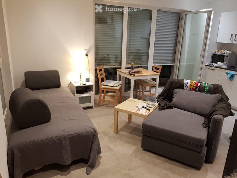 A compact, well-lit living space with a sofa, coffee table, dining table, chairs, and a microwave in the corner.