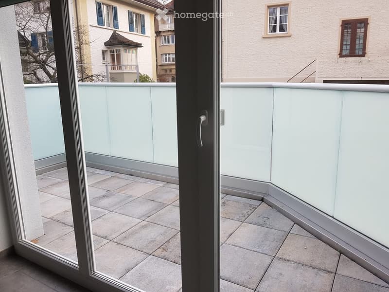 Balcony with tiled floor, glass railing, and view of neighboring buildings.