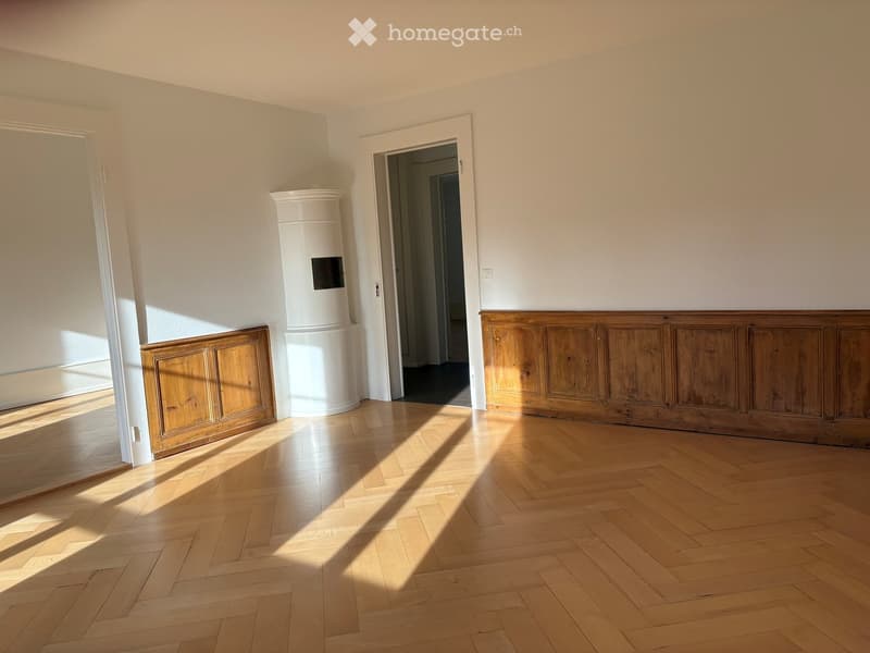 Empty room with wooden herringbone flooring, white walls, and a white cylindrical object in the center. Two doorways lead to adjacent spaces.