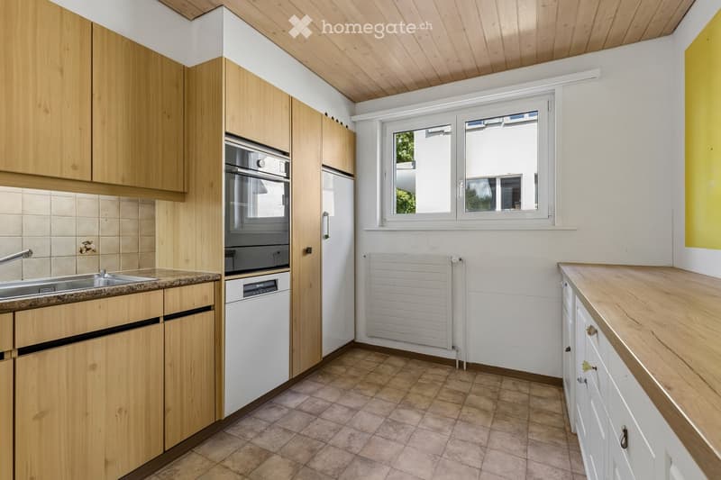 Modern kitchen with light wooden cabinets, stainless steel sink, oven, dishwasher, and a window providing natural light.