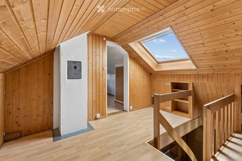 Bright, wooden-floored attic space with exposed wooden beams, skylight windows, and a small wooden staircase leading downwards.