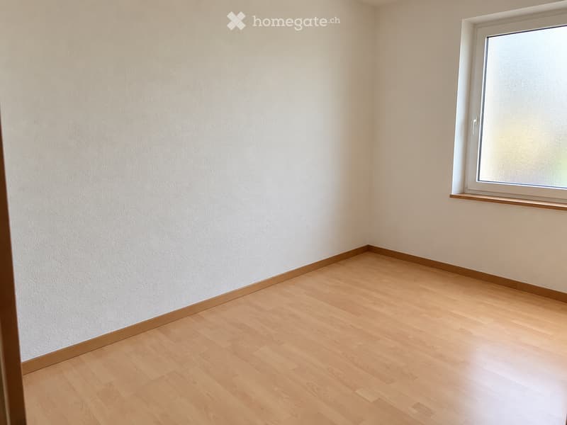 Empty room with light wooden flooring and white walls, featuring a single window with a white frame and a small wooden sill.