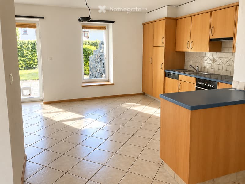 Bright kitchen with wooden cabinets, tiled floor, and a window overlooking a garden. Features a sink, faucet, and oven.