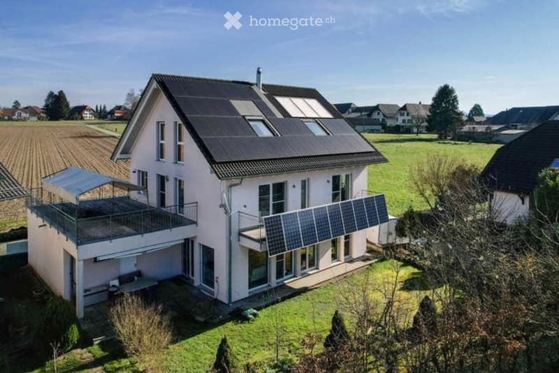 Two-story house with solar panels on the roof, balconies, and a covered outdoor seating area.