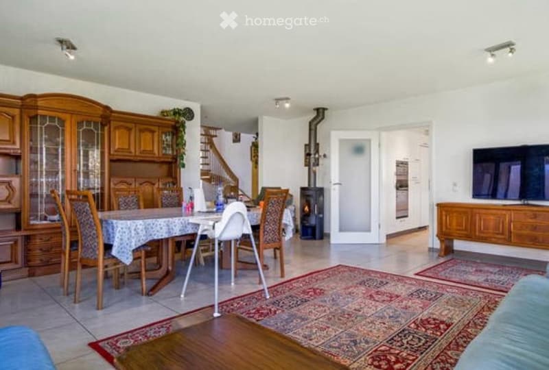Bright living and dining area with wooden furniture, a dining table with chairs, a TV, and a fireplace.