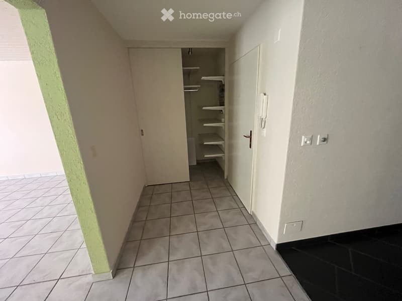 Empty hallway with tiled floor, white walls, and a closet with empty shelves.