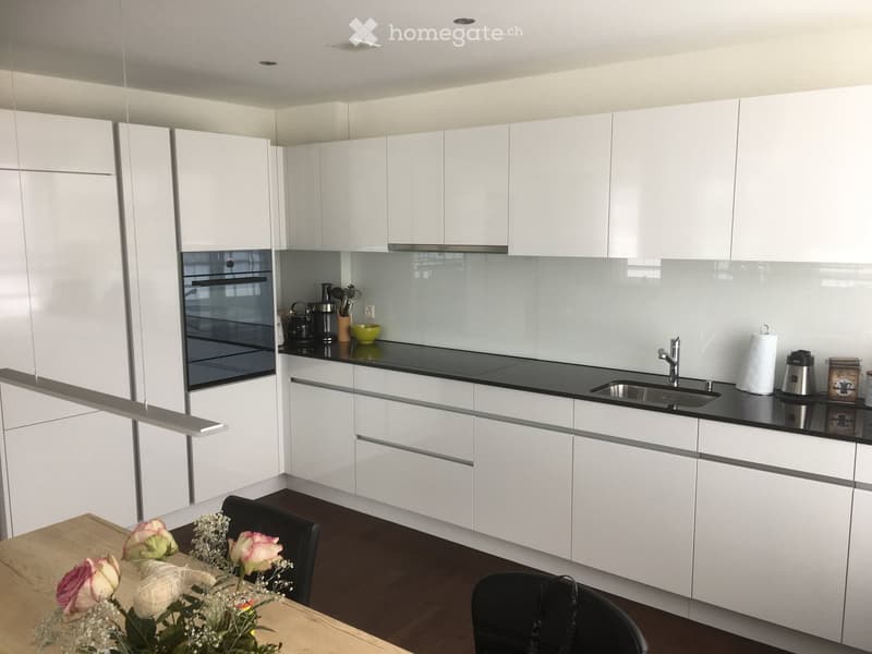 Modern kitchen with white cabinets, black countertops, and stainless steel appliances. Includes a sink, oven, and a small dining area with a table and chairs.