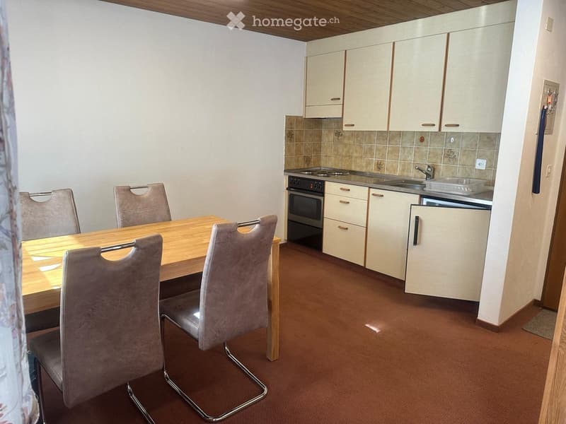 A compact kitchen and dining area with a wooden dining table, four chairs, white cabinets, a sink, and an oven.
