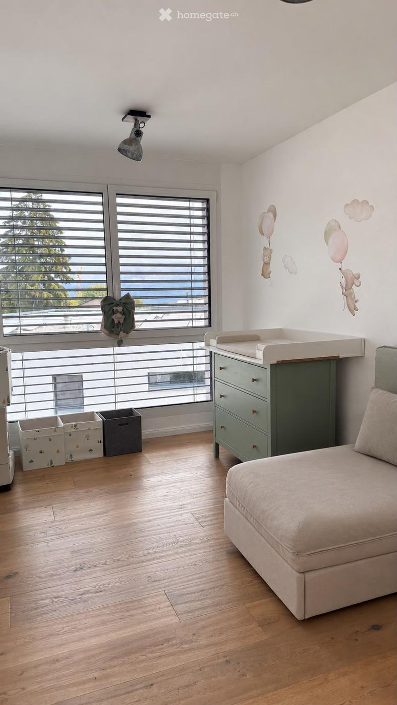 Bright, modern bedroom with wooden flooring, large windows with blinds, a sofa, changing table, drawer unit, and decorative wall decals.