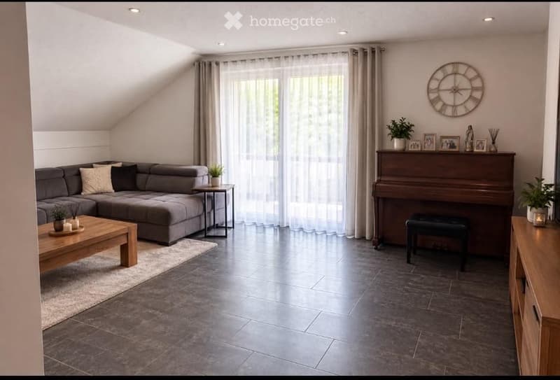 Modern living room with grey sectional sofa, wooden coffee table, side tables, piano, and decorative items including a large wall clock and potted plants.