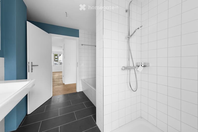 Modern bathroom with white tiles, black floor tiles, a white sink, a bathtub, and a shower with a handheld sprayer.